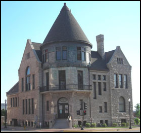 This Romanesque Revival style building, designed by Patton and Fisher in 1888, originally housed the Quincy Public Library. When the library vacated the building in 1974, John Willis Gardner bought the building and established an architectural museum which opened in 1977.  Unique features include the large, three story, circular corner tower, extremely textured stone walls that contrast with smoother brick ones and ornamental iron railings and slate roofs.