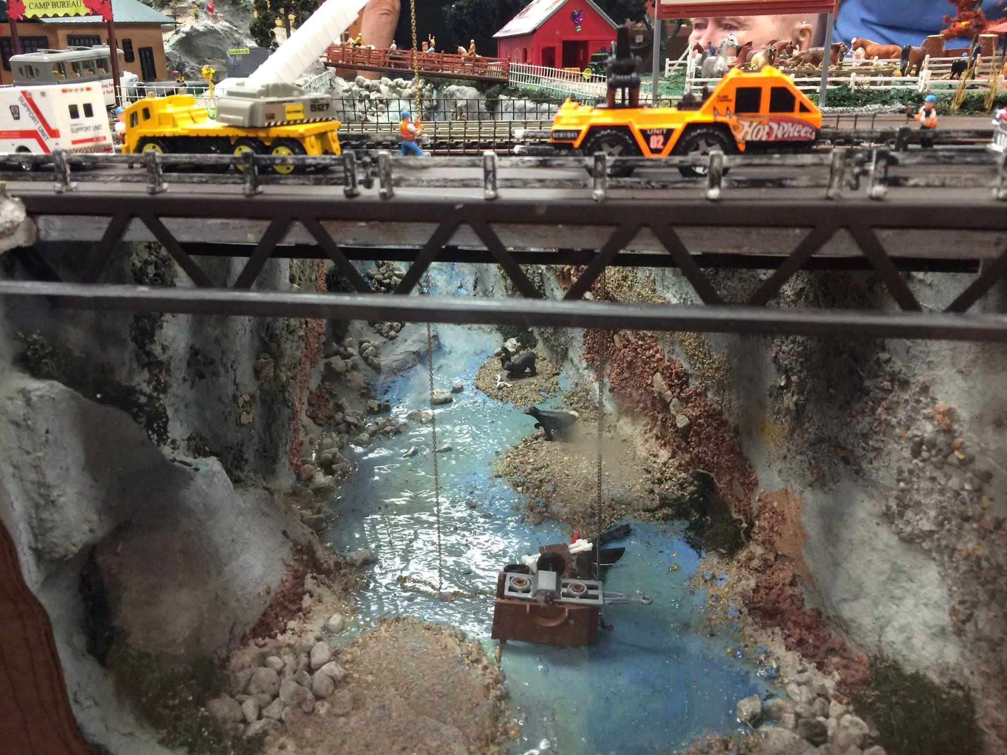 Model train layout with a canyon bridge, emergency vehicles, a rescue scene, and a river at Oshawa Pine Ridge Model Railroaders Club.