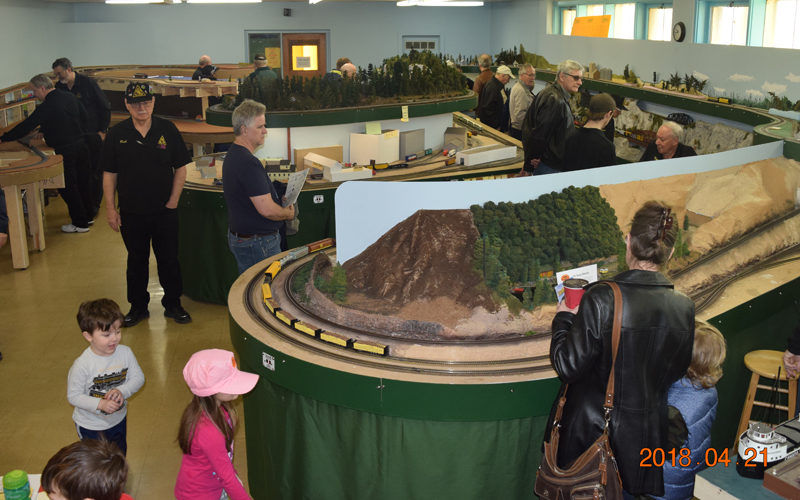 Visitors, including families and model train enthusiasts, explore an intricate railway layout at the Pine Ridge Model Railroaders Club open house.