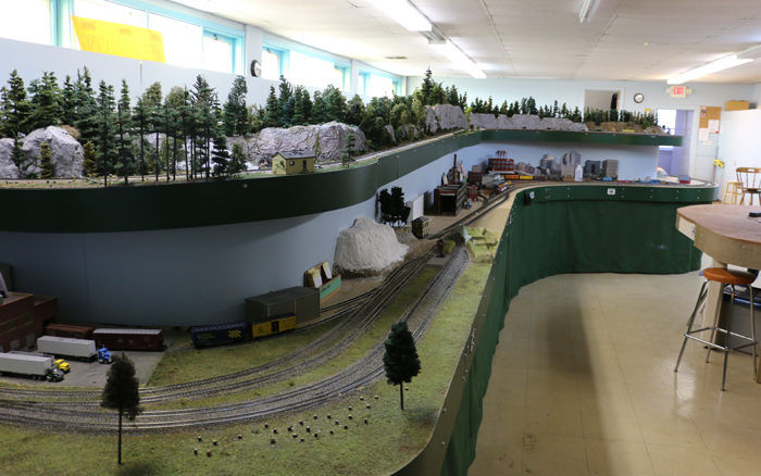 Multi-level model train layout at Pine Ridge Model Railroaders Club with forests, tracks, and an industrial scene.