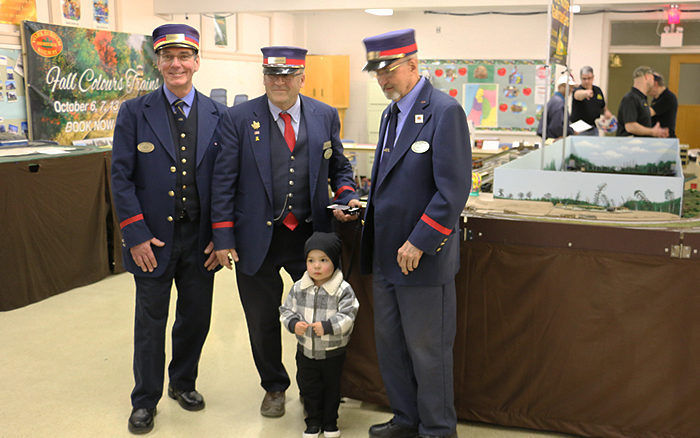 Three model railroad conductors in uniform with a young child at Pine Ridge Model Railroaders Club.