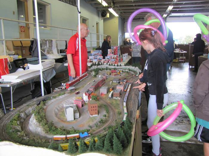 A young visitor interacts with a model train layout featuring a winding railway, miniature buildings, and landscapes at a train exhibition.