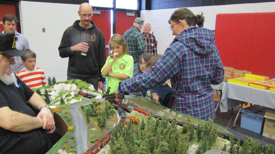 Visitors of all ages enjoy an interactive model train setup at the Oshawa Pine Ridge Model Railroaders Club, featuring detailed landscapes and locomotives.