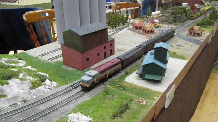 Model railroad scene at Oshawa Pine Ridge Model Railroaders Club with a Canadian Pacific passenger train passing by an industrial grain elevator and small-town structures.