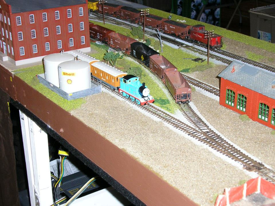 Thomas the Tank Engine model train on a detailed railway layout with freight cars, buildings, and Shell fuel tanks at the Oshawa Pine Ridge Model Railroaders Club.
