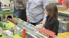 A detailed model railway featuring a train yard, multiple tracks, and a control tower.