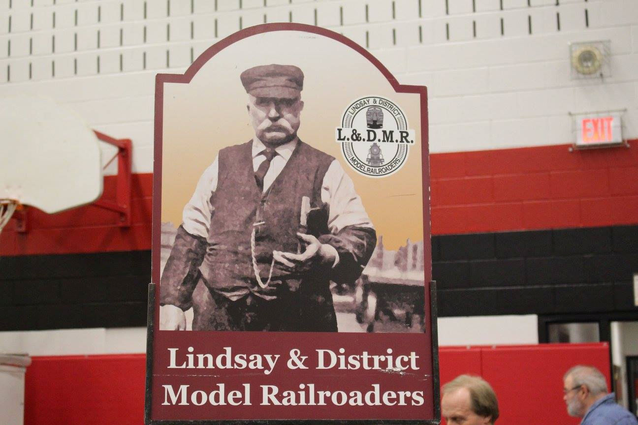 Lindsay & District Model Railroaders sign with a vintage railway worker illustration at a model train event.