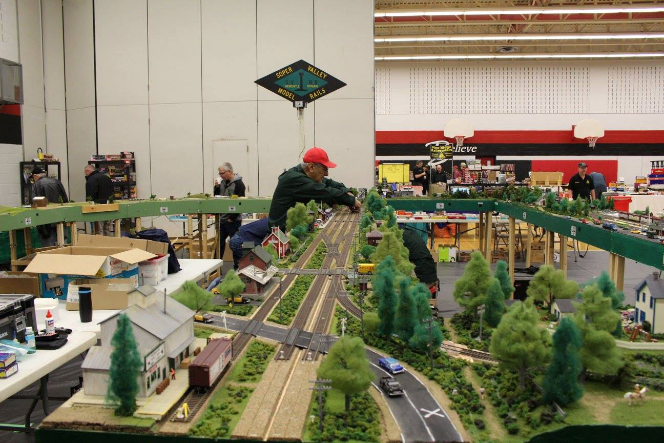Enthusiast working on a detailed model train setup featuring a small town, greenery, and railway tracks.
