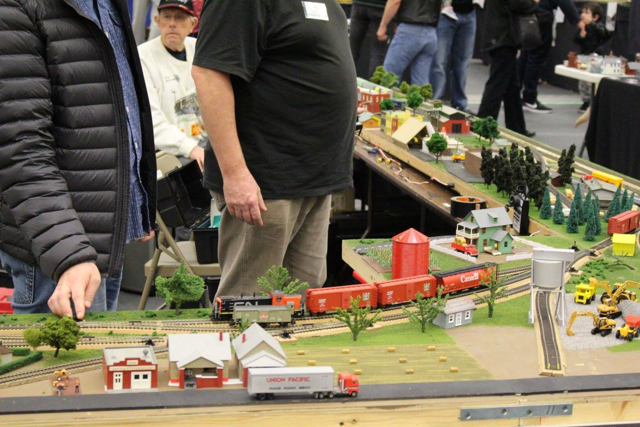A model train layout with a Canadian train, houses, silos, and construction equipment at a model railroad event.