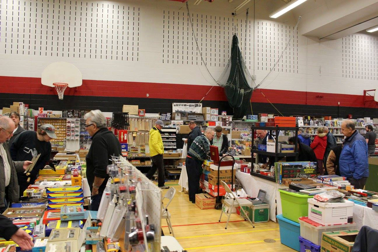 Train show attendees exploring vendor booths with model trains, scenery supplies, and railroad memorabilia.