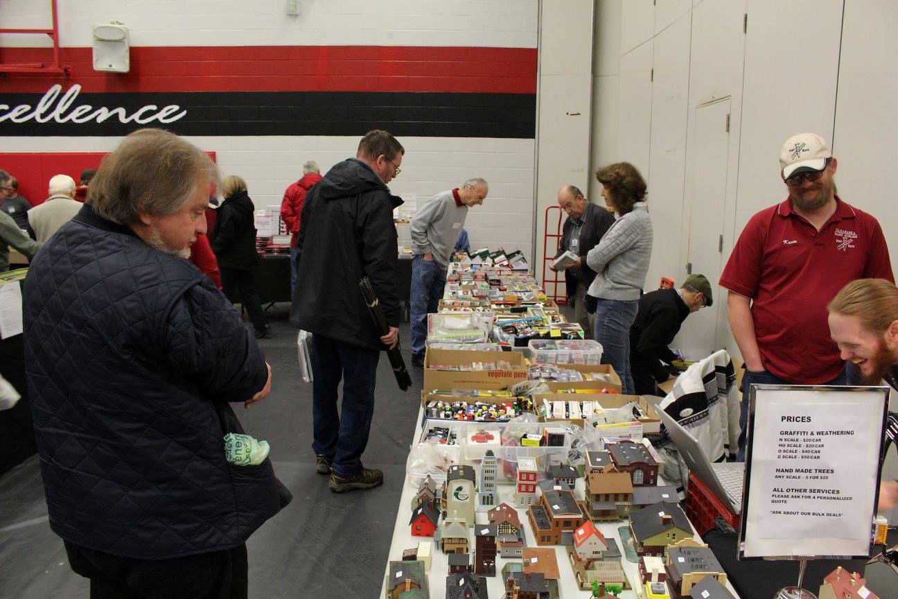 Attendees exploring model train supplies, including buildings and trains, at a Pine Ridge Model Railroaders Club event.