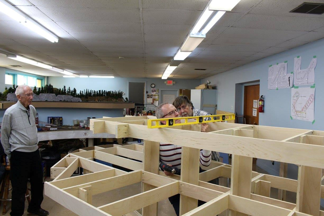 Club members using a level to ensure precision while building a wooden framework for a model railroad display.