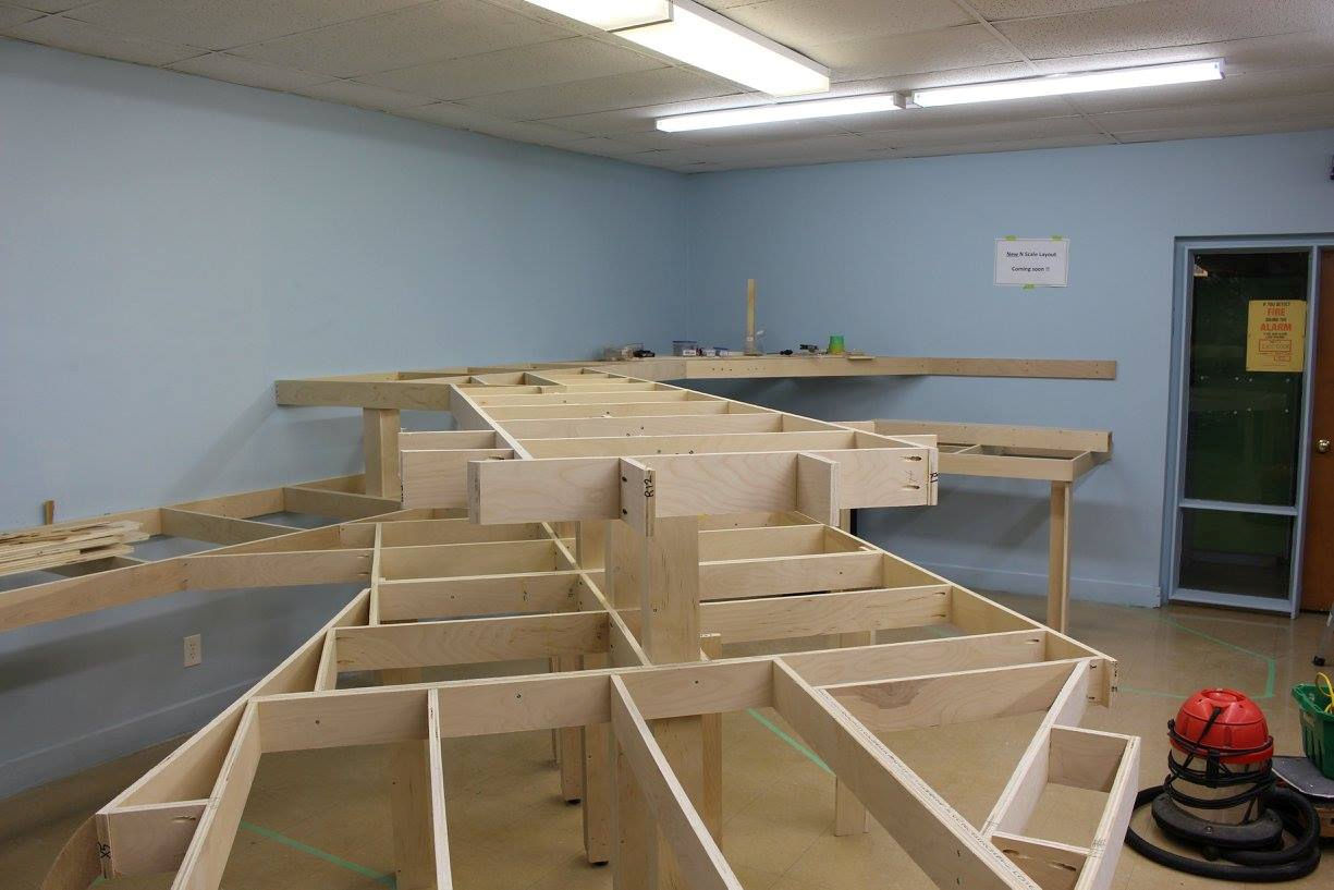 Wooden model railroad benchwork under construction in a workshop setting.