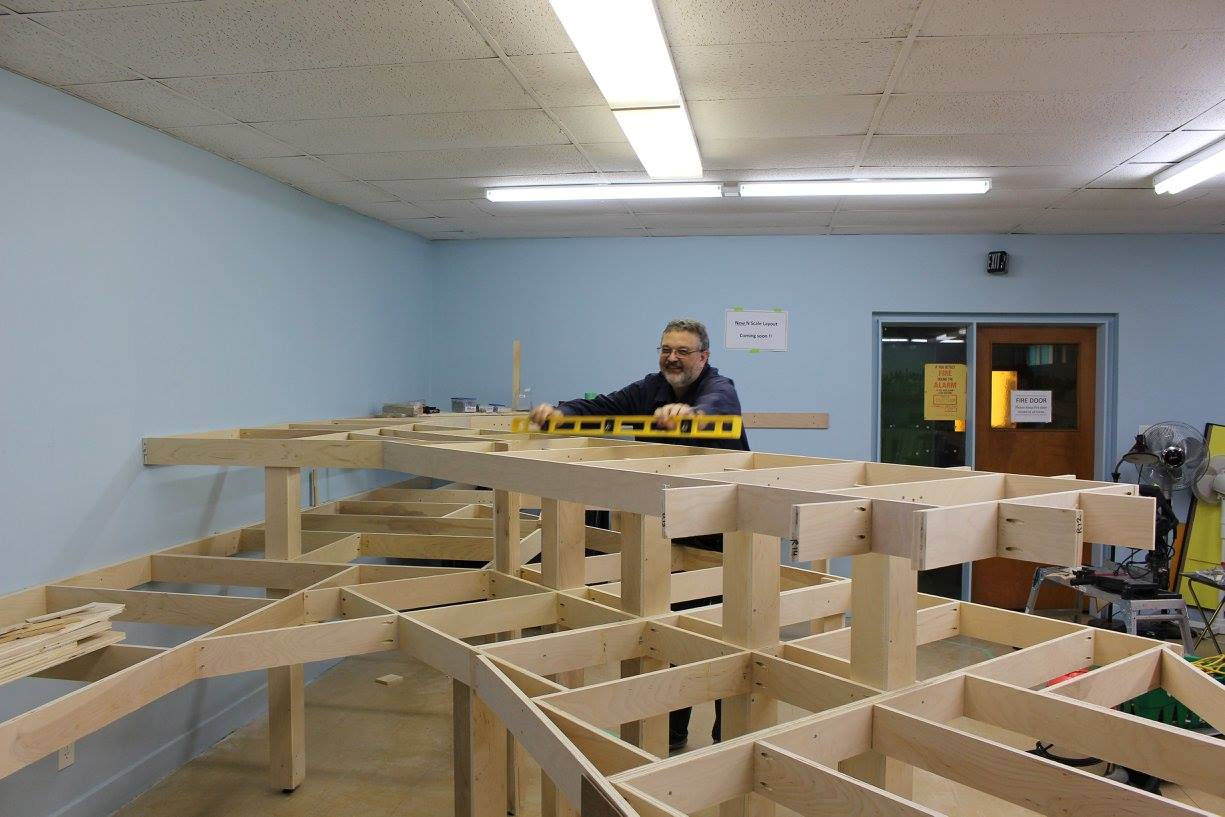 Man using a level to ensure accuracy while building model railroad benchwork.