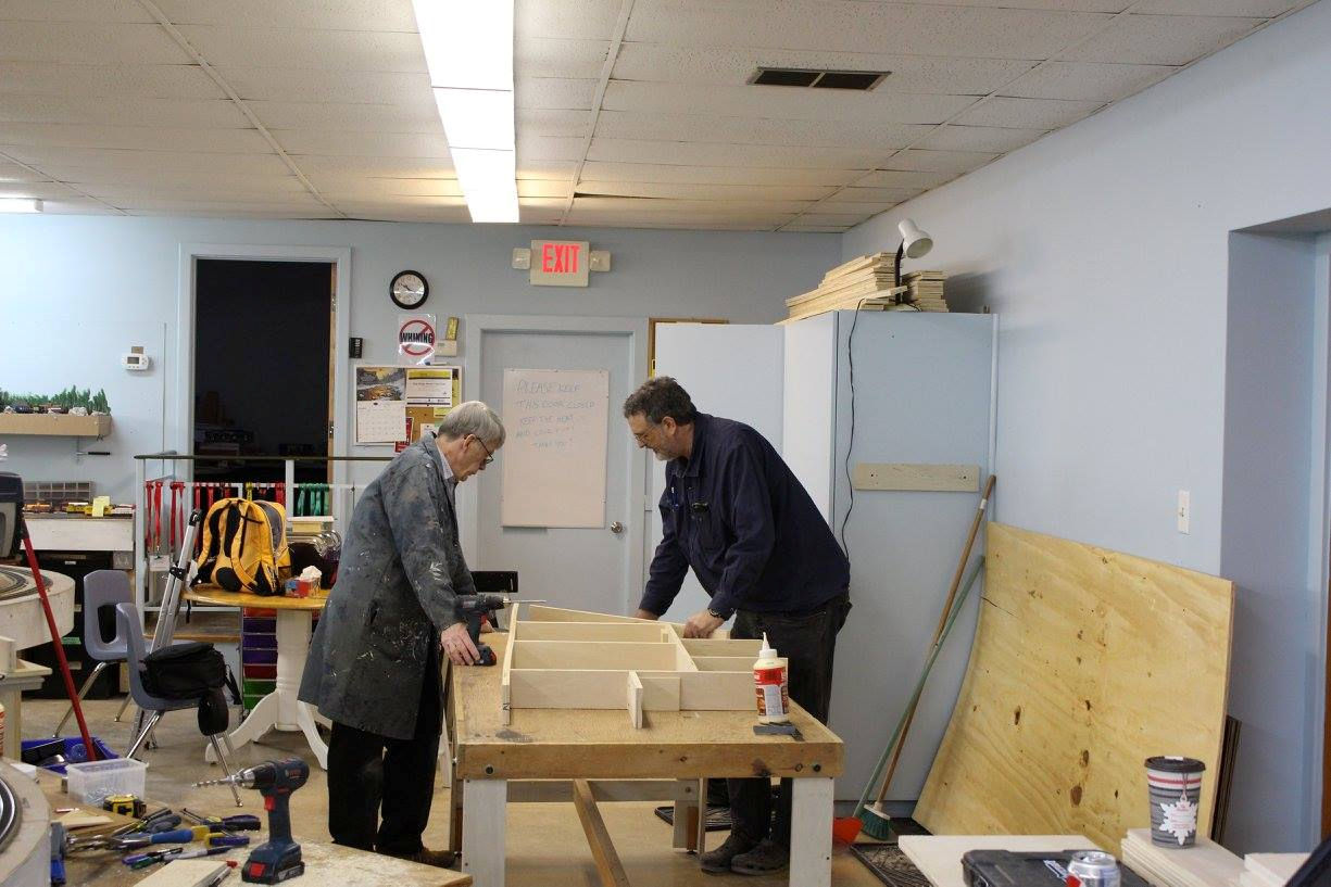 Two model railroaders assembling a wooden train layout structure.