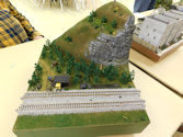 A detailed model railway featuring a freight train crossing a scenic trestle bridge.