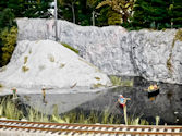 A model railway with a detailed train station, multiple tracks, and waiting passengers.